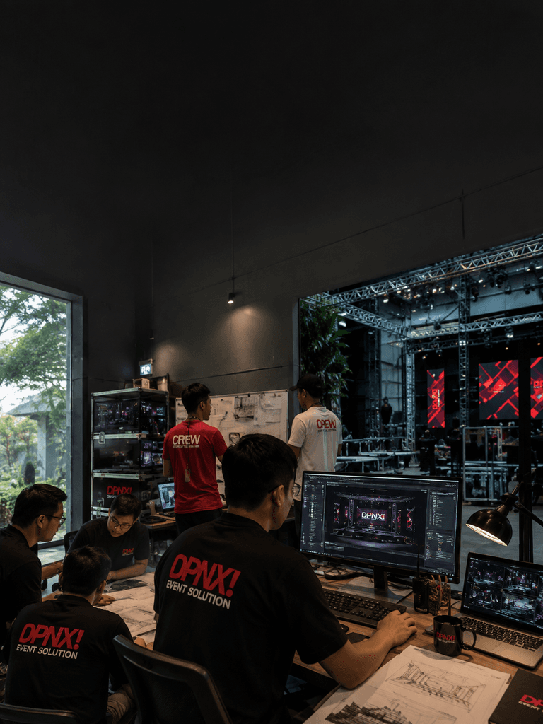 DPNX event production team reviewing stage designs at workstation with live stage setup visible in venue